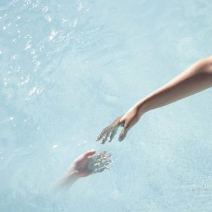 Touch - Reflection of a woman hand touching water. Illusion of two hands touching. Beach photography of blue, transparent still water.