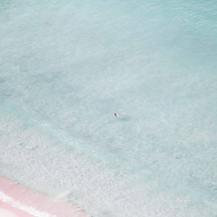 The Swimmer - Solo swimmer in crystal clear waters of the ocean. Light blue sea and dreamy pink sandy beach evokes the essence of summer.