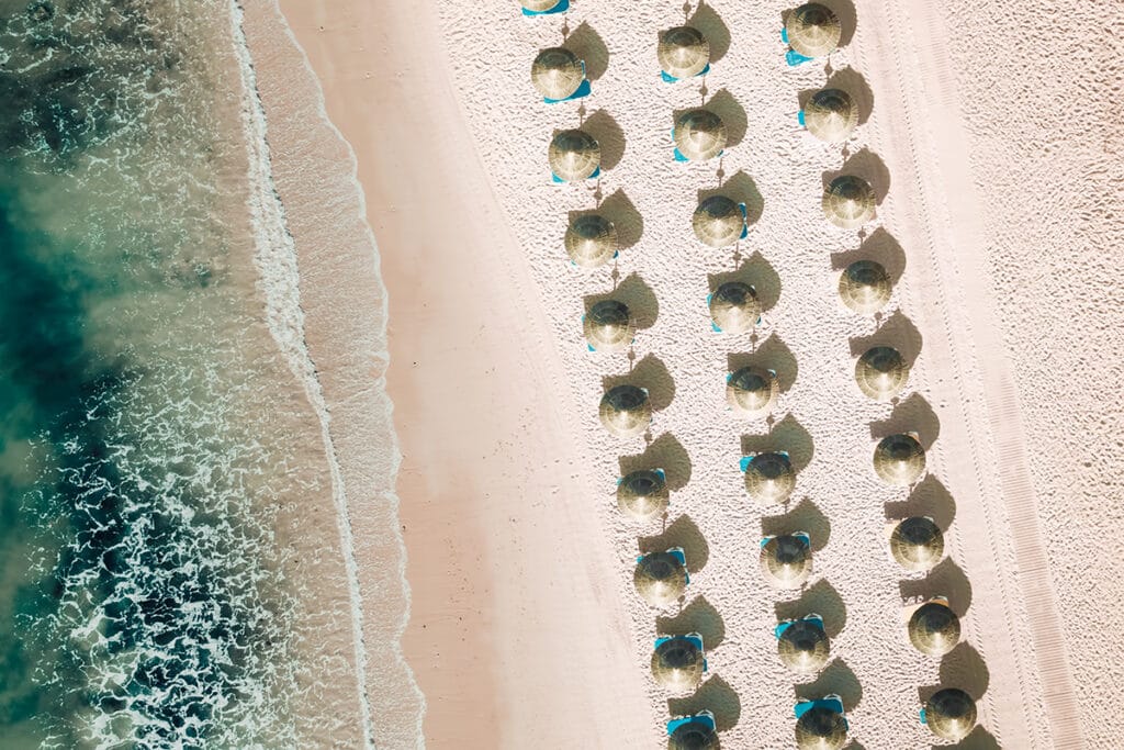 Aerial view of tropical beach with symmetrical straw umbrellas and turquoise waves