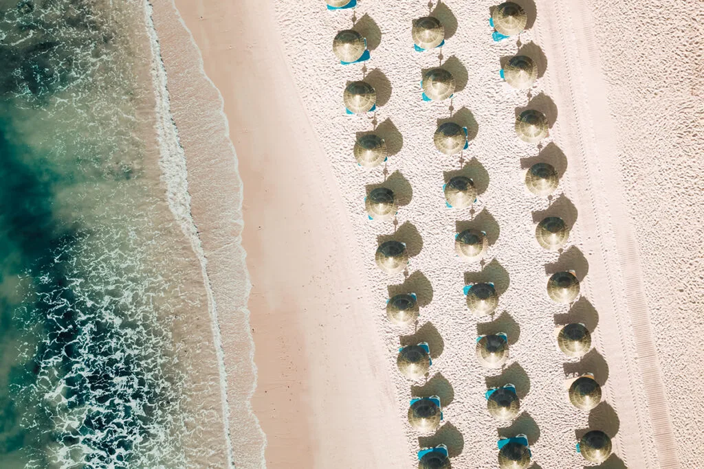 Aerial view of tropical beach with symmetrical straw umbrellas and turquoise waves