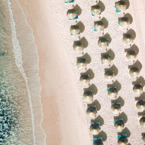Aerial view of tropical beach with symmetrical straw umbrellas and turquoise waves
