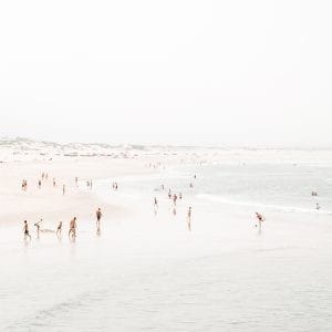 Aerial beach photo of people walking and playing along a soft pastel shoreline with gentle waves.