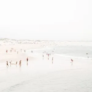 Aerial beach photo of people walking and playing along a soft pastel shoreline with gentle waves.