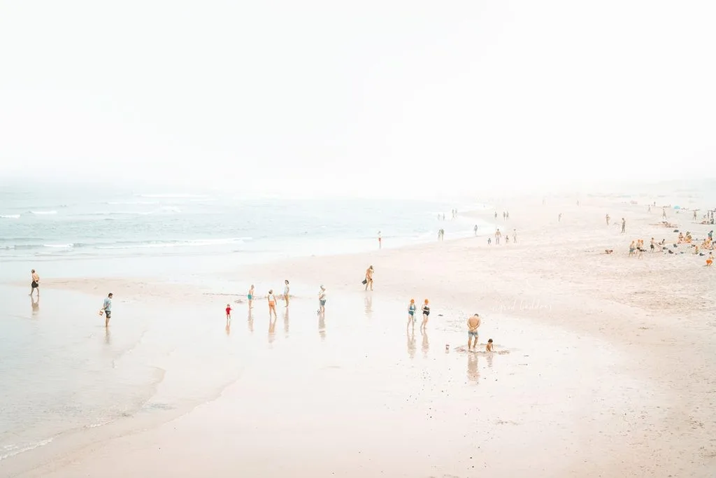 Aerial beach photograph with families and beachgoers scattered across soft wet sand near gentle surf.