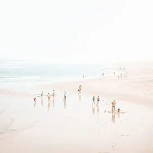 Aerial beach photograph with families and beachgoers scattered across soft wet sand near gentle surf.