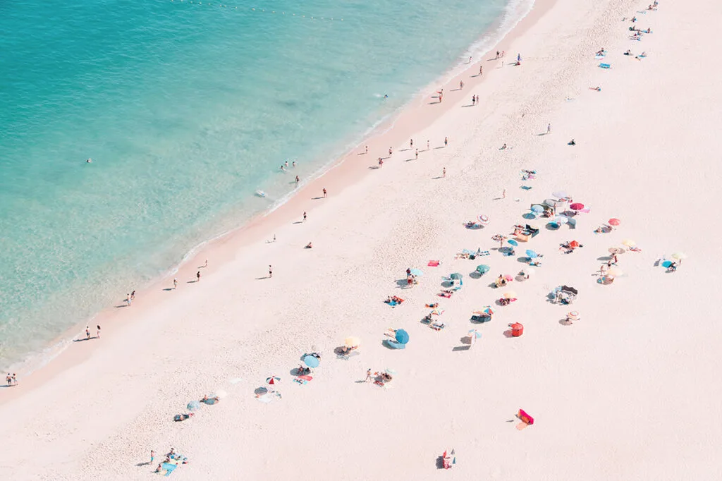 Crowded beach with colorful umbrellas and swimmers in turquoise sea seen from above