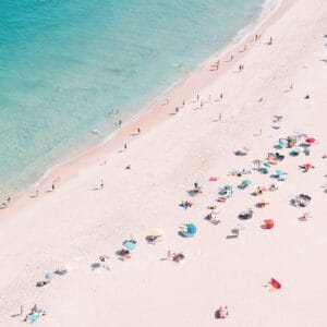 Crowded beach with colorful umbrellas and swimmers in turquoise sea seen from above