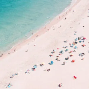 Crowded beach with colorful umbrellas and swimmers in turquoise sea seen from above
