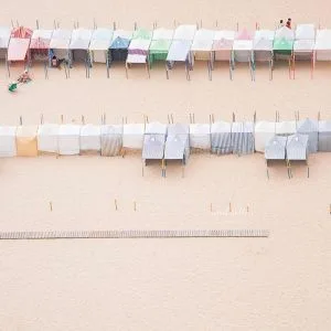 Rows of pastel beach huts lined up on a sandy beach, captured from above