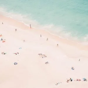 Aerial shot of people scattered along a peaceful, pastel-toned beach and aqua sea