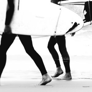 Black and white photo of surfers walking barefoot on the sand carrying surfboards.