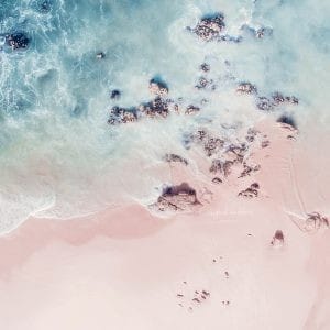 Aerial photo of rocky shoreline with soft blue waves crashing on a sandy beach