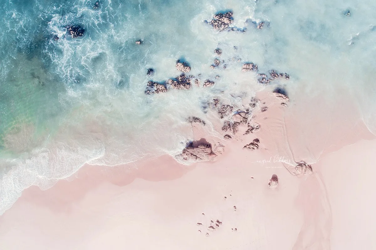 Aerial photo of rocky shoreline with soft blue waves crashing on a sandy beach