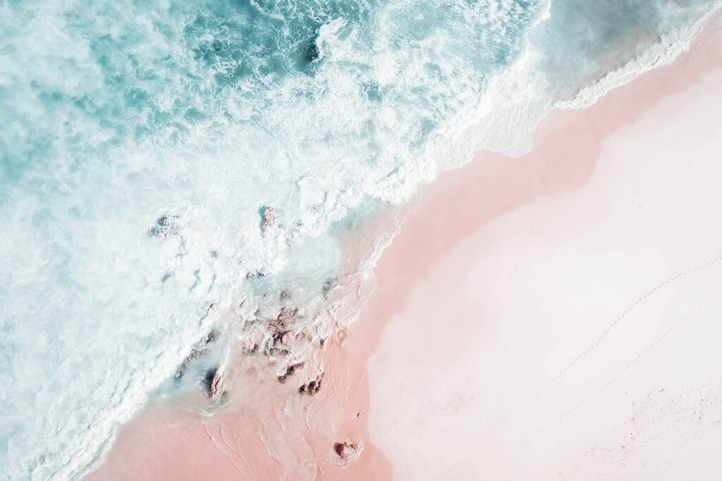 Drone photo of pink sand beach and foamy turquoise waves crashing over rocks