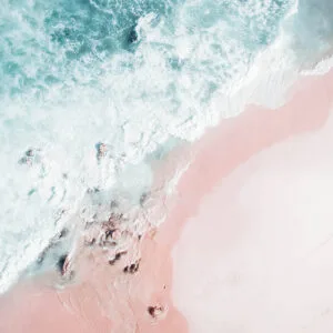 Drone photo of pink sand beach and foamy turquoise waves crashing over rocks