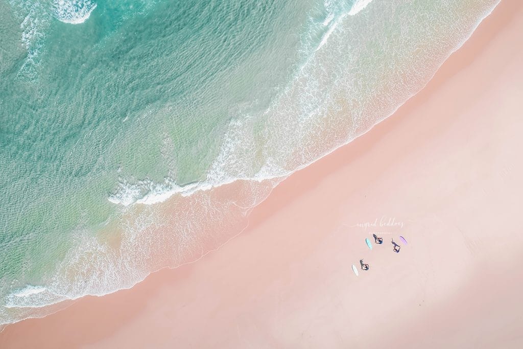Aerial photo of surfers practicing yoga on the sand next to turquoise waves