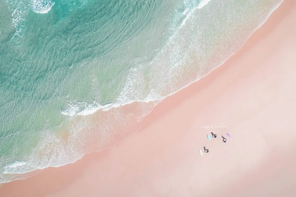 Aerial photo of surfers practicing yoga on the sand next to turquoise waves