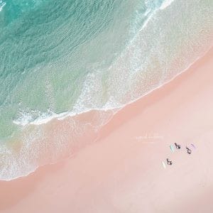 Aerial photo of surfers practicing yoga on the sand next to turquoise waves