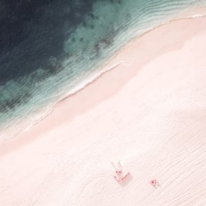 Aerial photo of a couple relaxing on a pinkish beach near emerald waters
