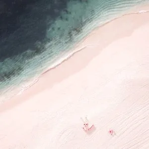 Aerial photo of a couple relaxing on a pinkish beach near emerald waters