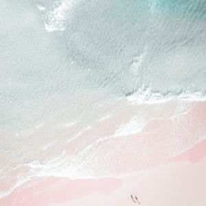 Aerial view of two people walking along a quiet pastel beach with gentle waves