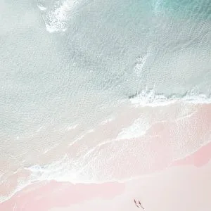 Aerial view of two people walking along a quiet pastel beach with gentle waves